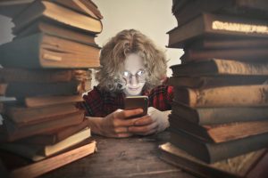 Student on smartphone, surrounded by stacks of books