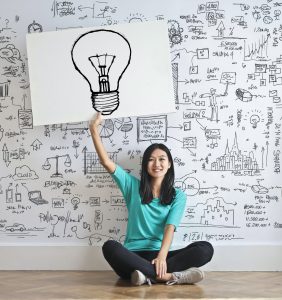 Woman sitting on the floor holding a poster with a lightbulb drawn on it