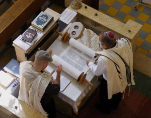 color photograph of two men in yamakas review a scroll, presumably the Torah