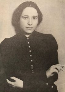 Sepia toned photograph of Hannah Arendt with her arms crossed and a cigarette in her right hand.