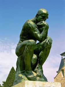 statue of a man seated on a rock, with his chin resting on his fist in a standard thinking pose