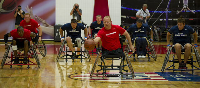 Seven men who have leg disabilities playing basketball in wheelchairs.