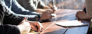close up of four men leaning on a table with pens and notepads