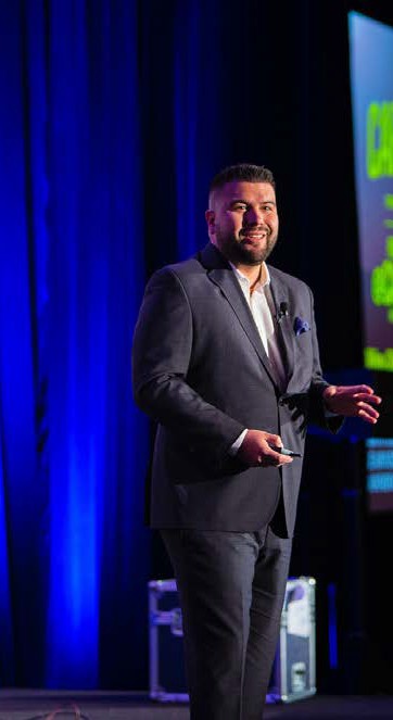 image of a man in a business suit standing on a stage behind a bright blue stage curatin
