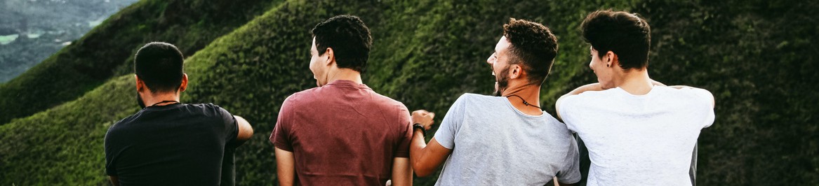 image of the back of four young men laughing as they stand on the top of a tall hill