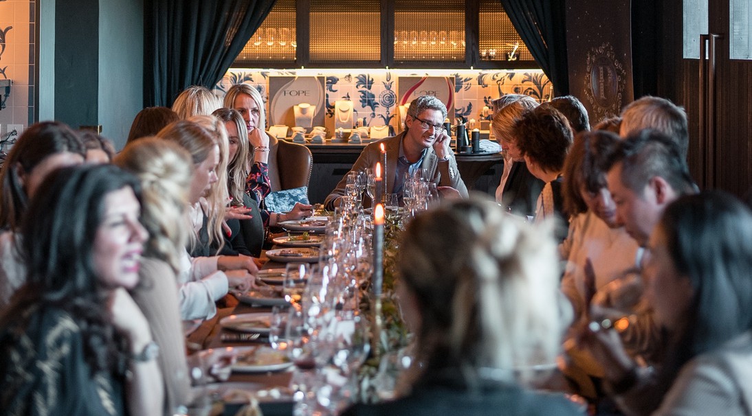 image of large dining table with dozens of people eating and talking