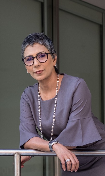 image of a woman wearing business casual dress looking at the camera while leaning foroward on a metal rail